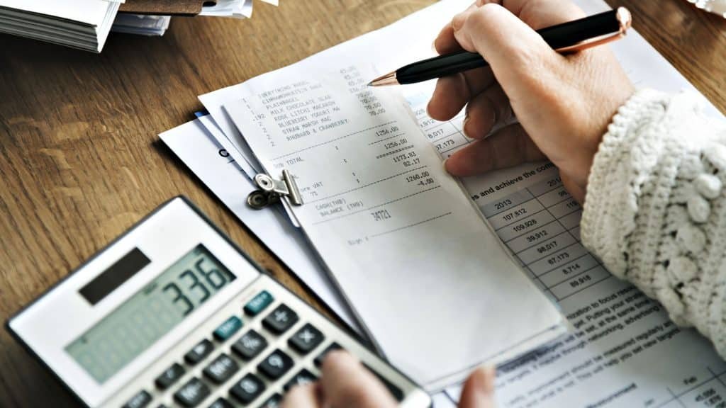 Person calculating finances with receipts and calculator on desk